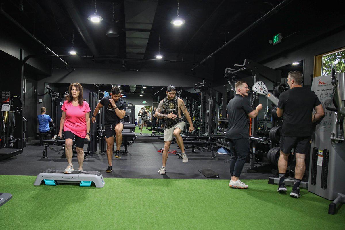Clients engaged in a dynamic workout session at Optimum Peak Fitness, performing strength and mobility exercises with guided support in a state-of-the-art training facility.