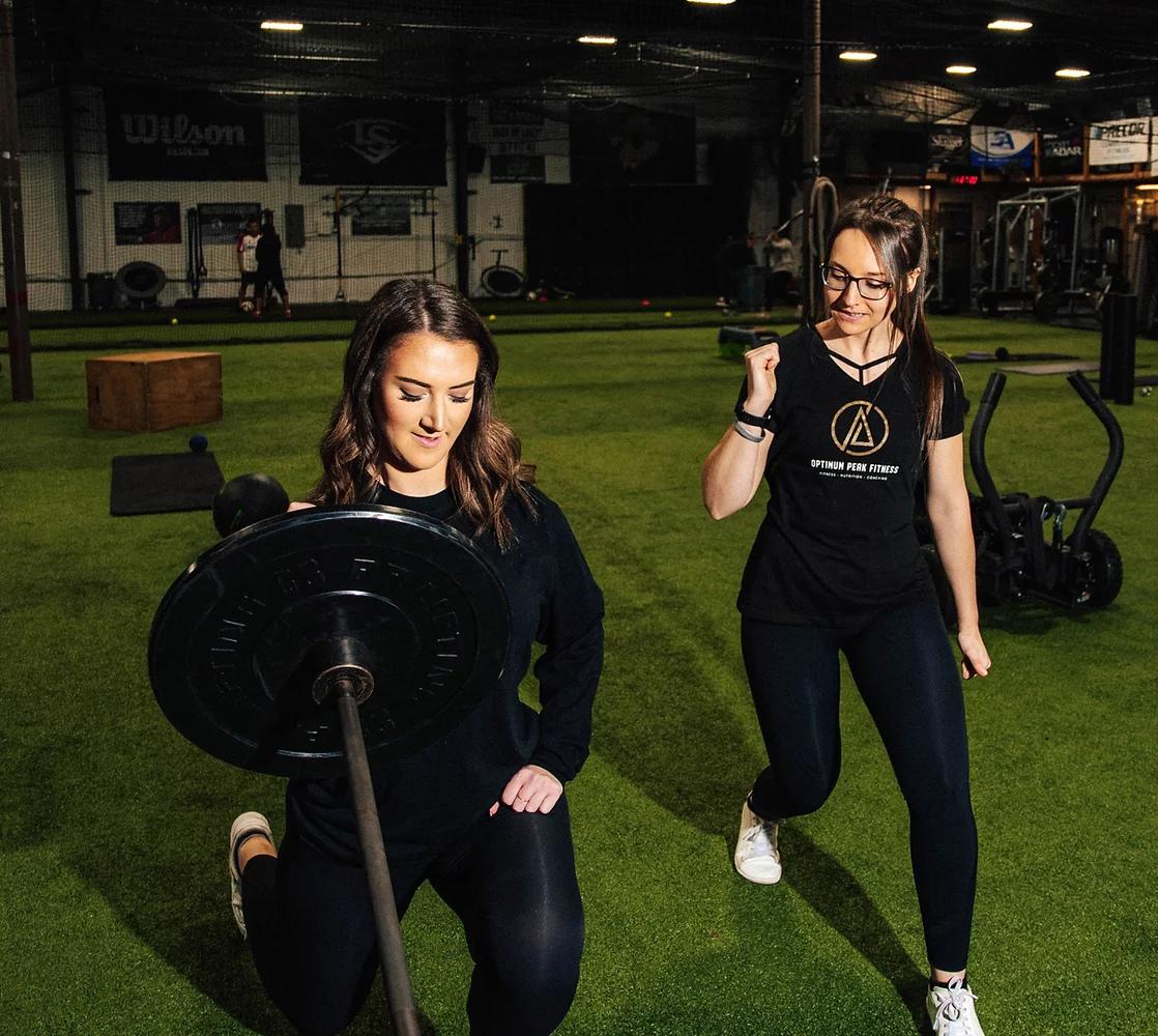 Female client performing a TRX suspension push-up under trainer supervision at Optimum Peak Fitness, building upper body strength and core stability in a functional training zone.